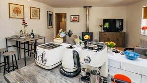 A modern kitchen with a built-in stove, a dining area with a table set for two, and a television on a wooden cabinet. - Muddy Boots – Scarpa. (Kirkby Stephen)