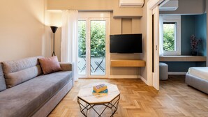 Een moderne woonkamer met een bank, een salontafel met boeken, een flatscreen televisie en een balkon met uitzicht op groen.