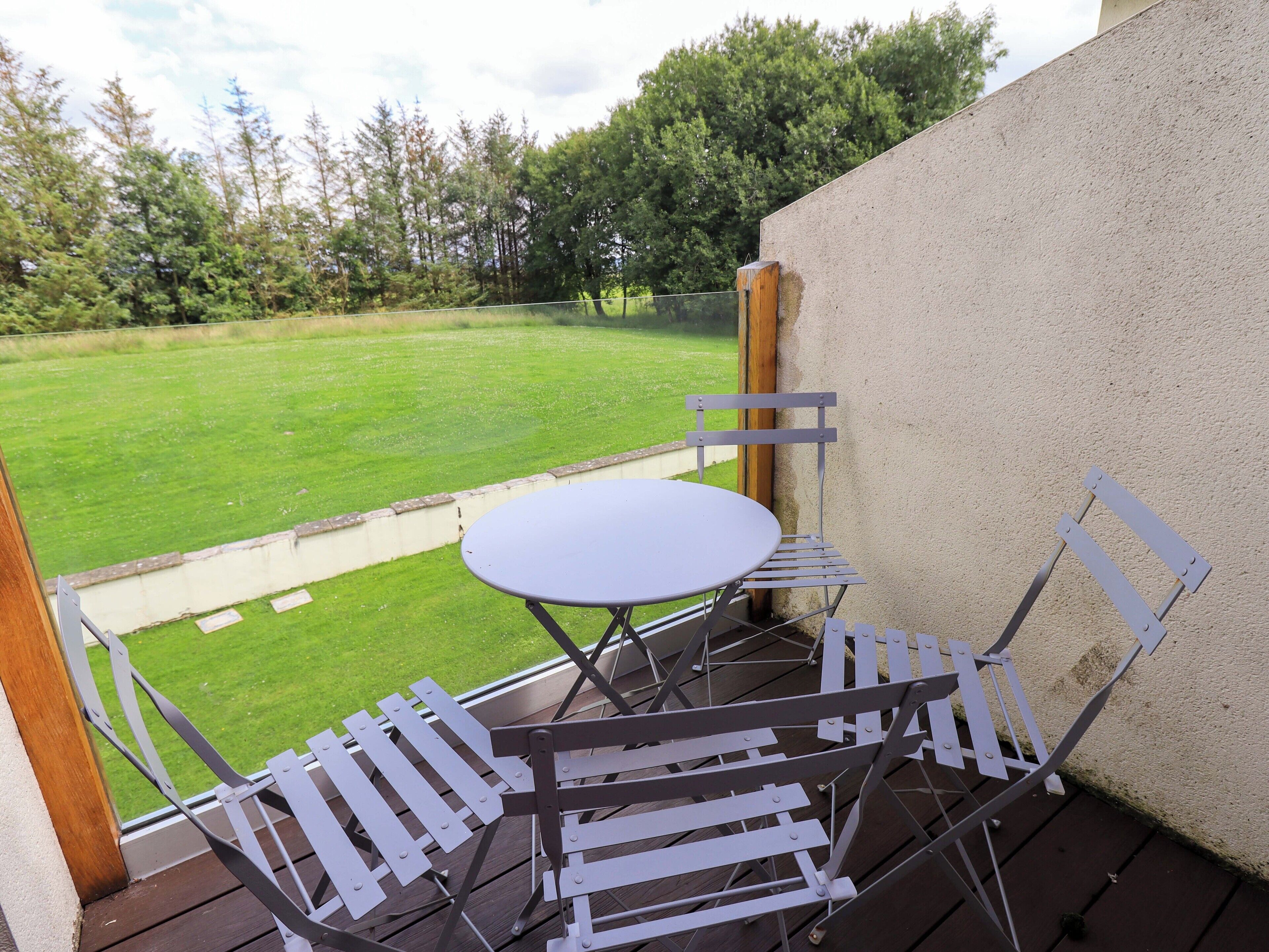 A patio with a round table and white metal chairs, overlooking a grassy lawn.