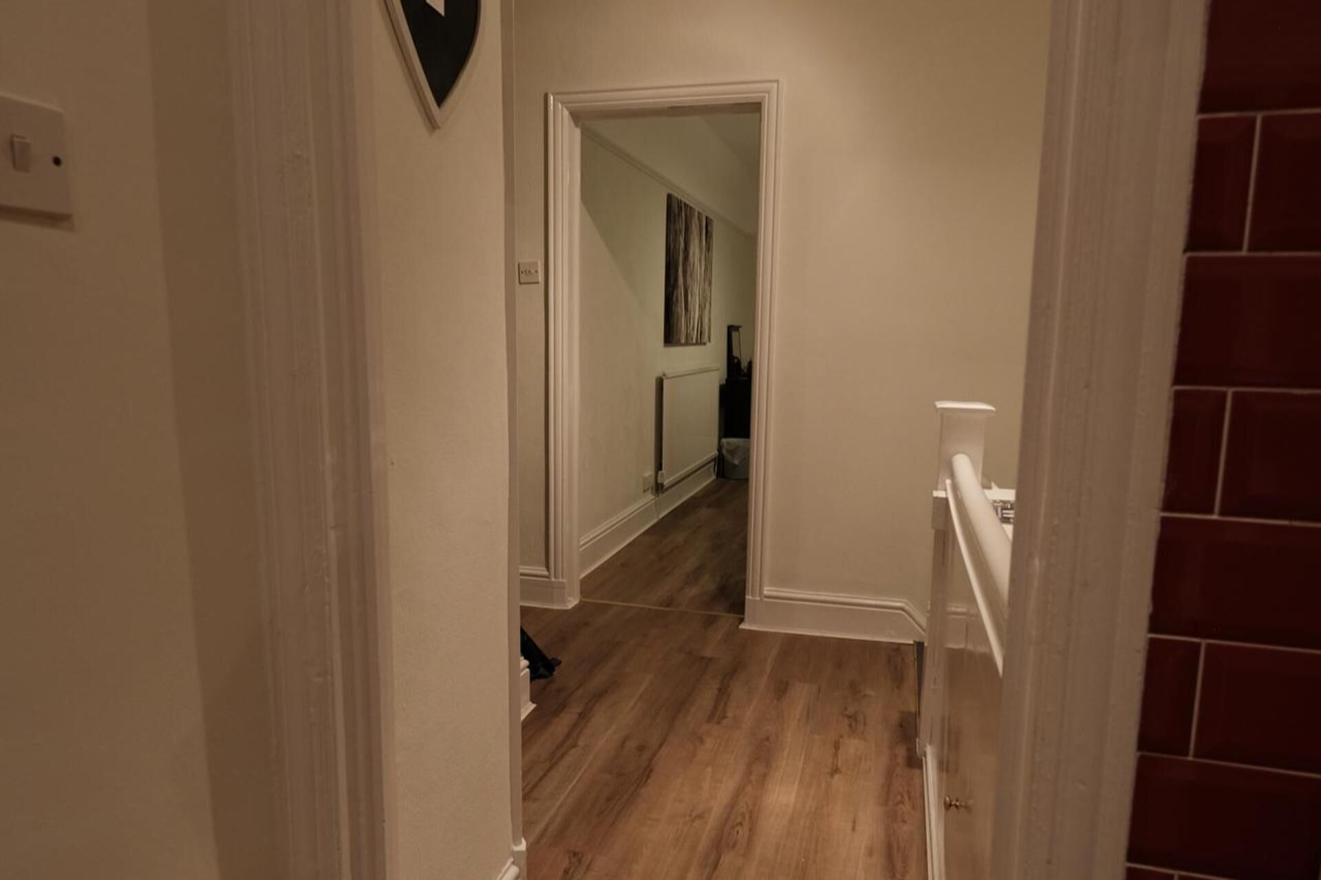 Un pasillo con suelo de madera, una puerta blanca y una pared de ladrillo rojo.