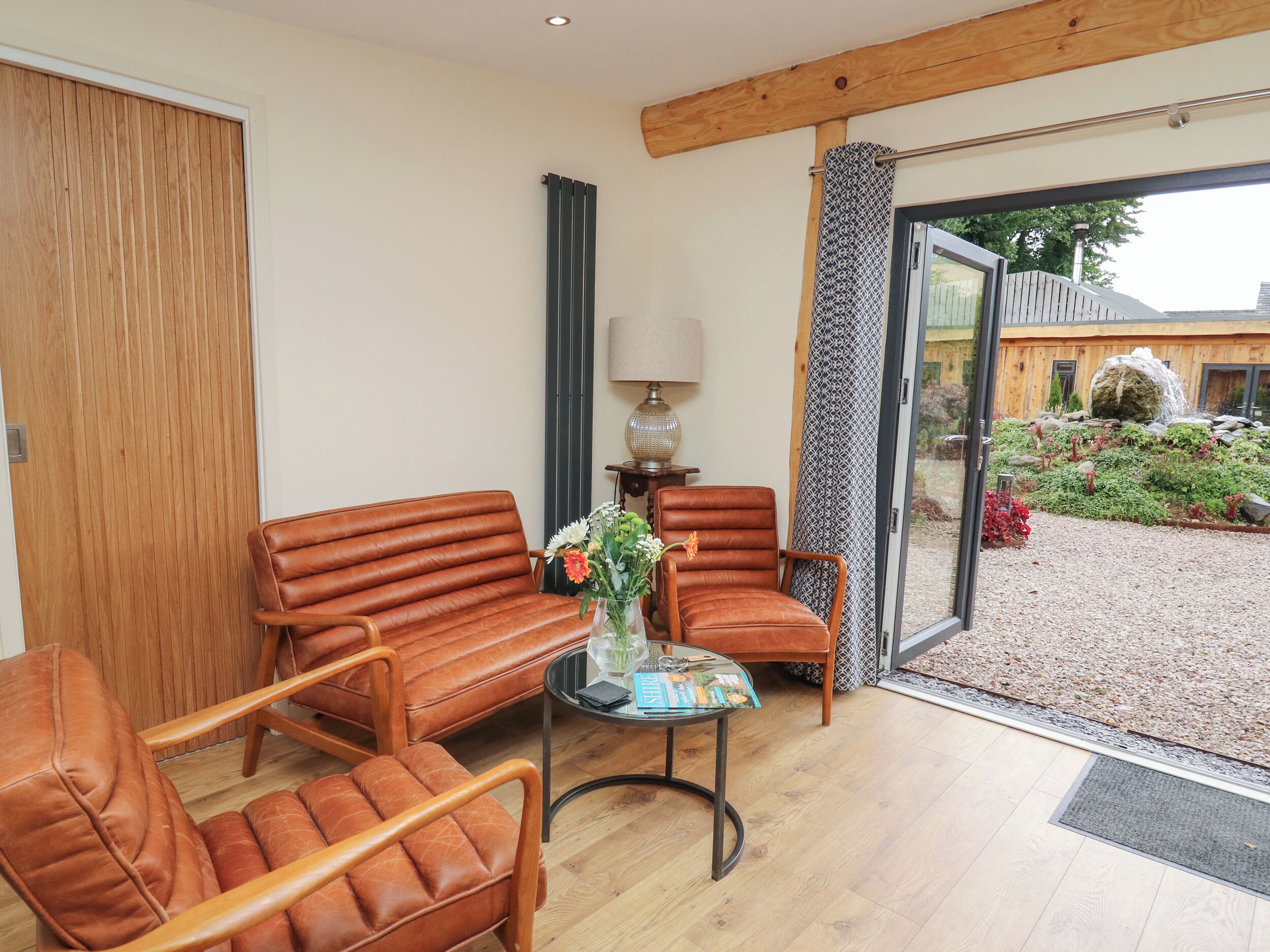A modern living room with leather sofas, a glass coffee table, and a view of a garden through a sliding glass door.