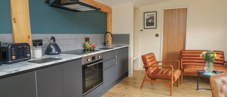 A modern kitchen with grey cabinets, a built-in oven, and a stainless steel range hood. There is a wooden dining table with two chairs and a vase of flowers.