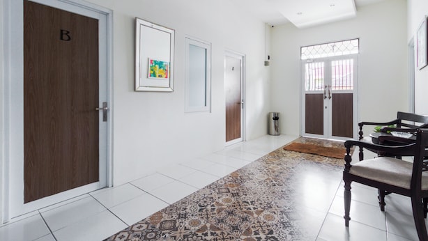 A hallway with a patterned rug, a wooden door labeled 'B', and a dining area with a chair and table. - OYO 2975 House Of Mahira Syariah (Baregbeg)
