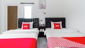 A hotel room with two beds, each with a red OYO pillow, a wooden door, a white wall, and a framed picture above the beds. - OYO 2975 House Of Mahira Syariah (Baregbeg)