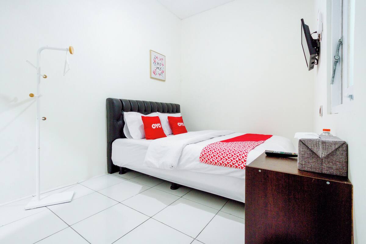 A neatly arranged bedroom with a bed, a bedside table, a wall-mounted light, and a framed picture.