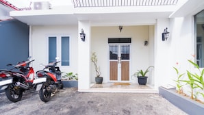 A building with a white facade, a wooden door, and two motorcycles parked in front. - OYO 2975 House Of Mahira Syariah (Baregbeg)