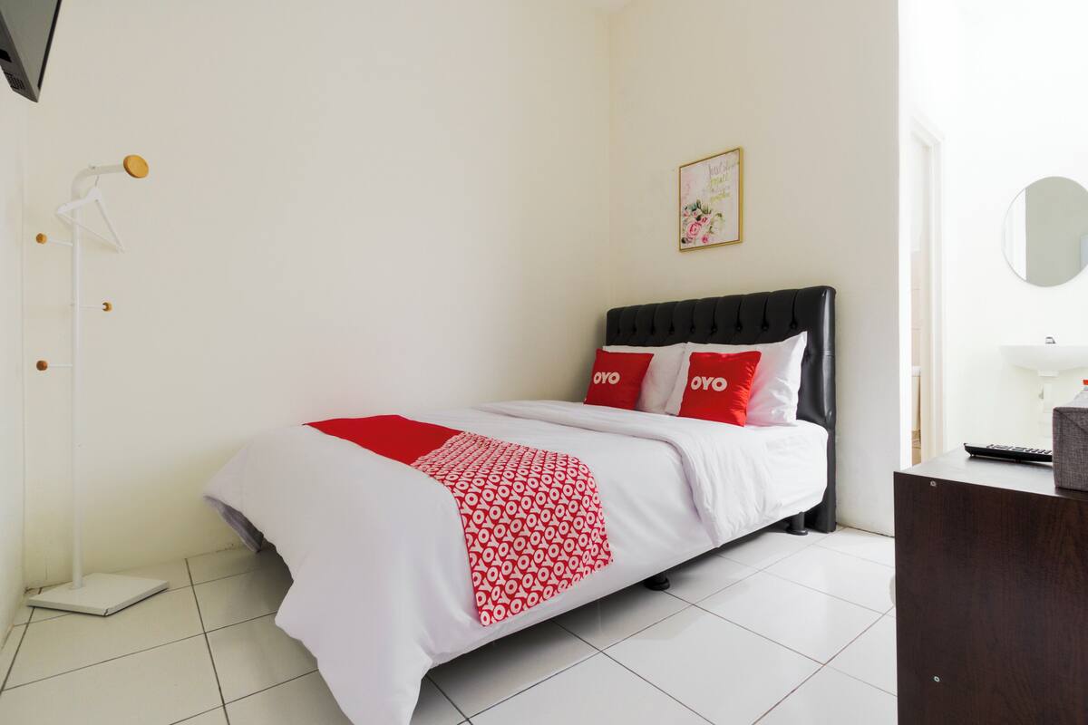 A neatly arranged bedroom with a bed, a bedside table, a mirror, and a wall-mounted shelf.