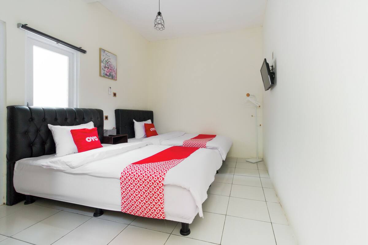 A hotel room with a large bed, two bedside tables, a flat-screen TV mounted on the wall, and a window with a curtain.
