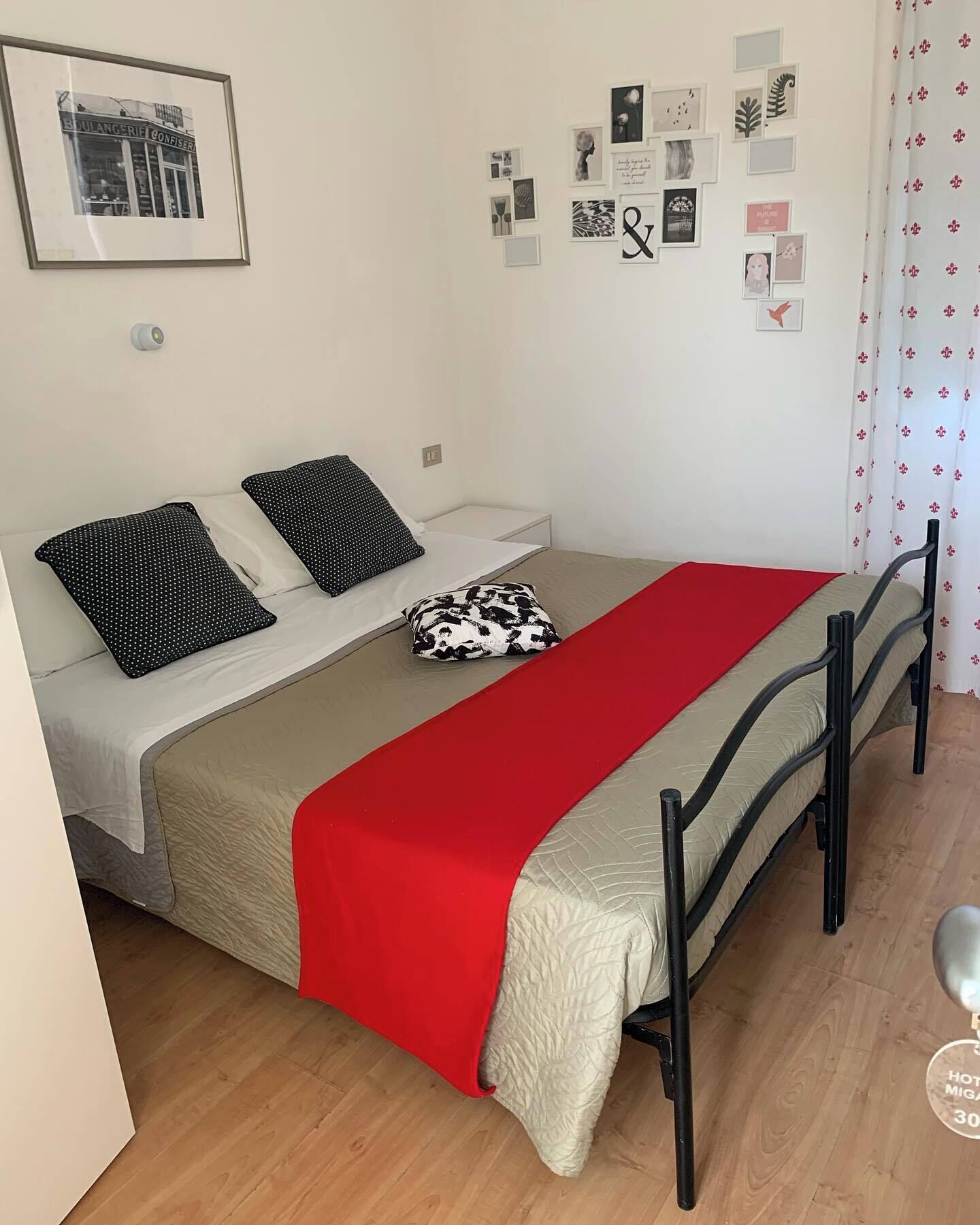 A single bed with a red blanket, two black and white pillows, and a small black and white bag on the bed.
