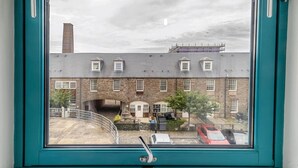 A view through a window of a building with a stone facade, a chimney, and a bridge. - Cozy Dundee Apartment With a View (Dundee)