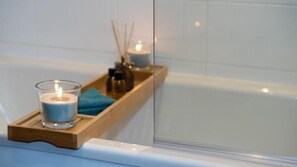 Un baño con una bandeja de madera que sostiene una vela y un portavelas de cristal.
