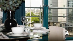A dining table set with plates, glasses, and a vase with flowers. A window reveals a cityscape with buildings and a car. - Cozy Dundee Apartment With a View (Dundee)