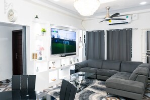 Uma sala de estar moderna com um sofá seccional, uma mesa de centro de vidro e uma TV de tela plana fixada na parede.