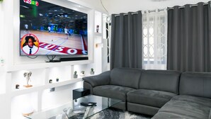 Un soggiorno moderno con una grande TV a schermo piatto montata a parete, un divano grigio e un tavolino da caffè in vetro.