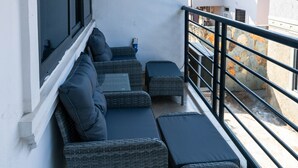 Un balcone con mobili in vimini, tra cui un divano e pouf, e una ringhiera.