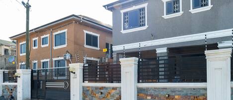 A residential area with two houses, one brown and one gray, with a gated driveway and a stone wall.