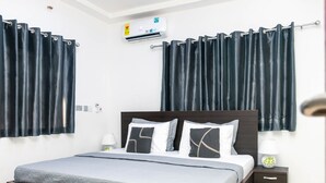 Una camera da letto con un letto, tende scure, un condizionatore d'aria, un comodino con una lampada e un tappeto decorato.