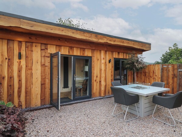 A wooden cabin with a glass door leading to a room, a table with chairs, and a gravel patio.