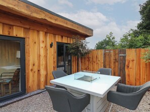 A modern outdoor patio with a glass-top table and four chairs, surrounded by wooden walls and a gravel ground.