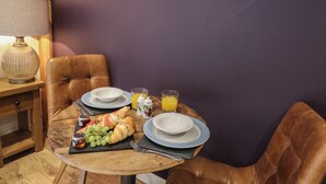 A breakfast setting with a wooden table, two plates, a glass of orange juice, croissants, and a fruit platter. - Daffodil (Welshpool)