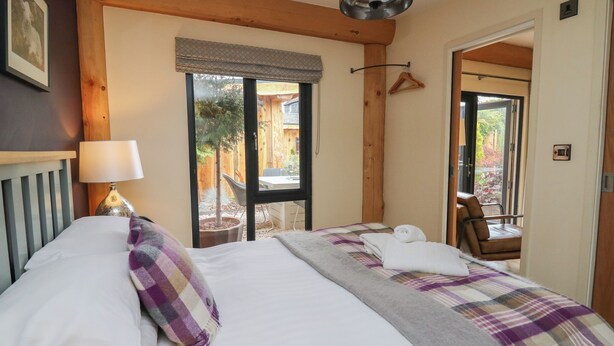 A bedroom with a bed, a hanging lamp, a window with a view of the outside, and a door leading to another room. - Daffodil (Welshpool)