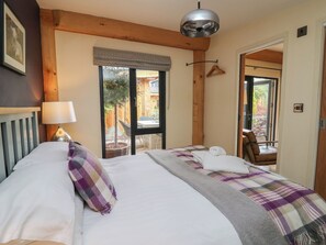 A bedroom with a bed, a hanging lamp, a window with a view of the outside, and a door leading to another room.