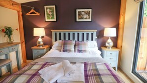 A bedroom with a bed, two bedside tables, a wooden headboard, a window, and a wall with two framed pictures. - Daffodil (Welshpool)
