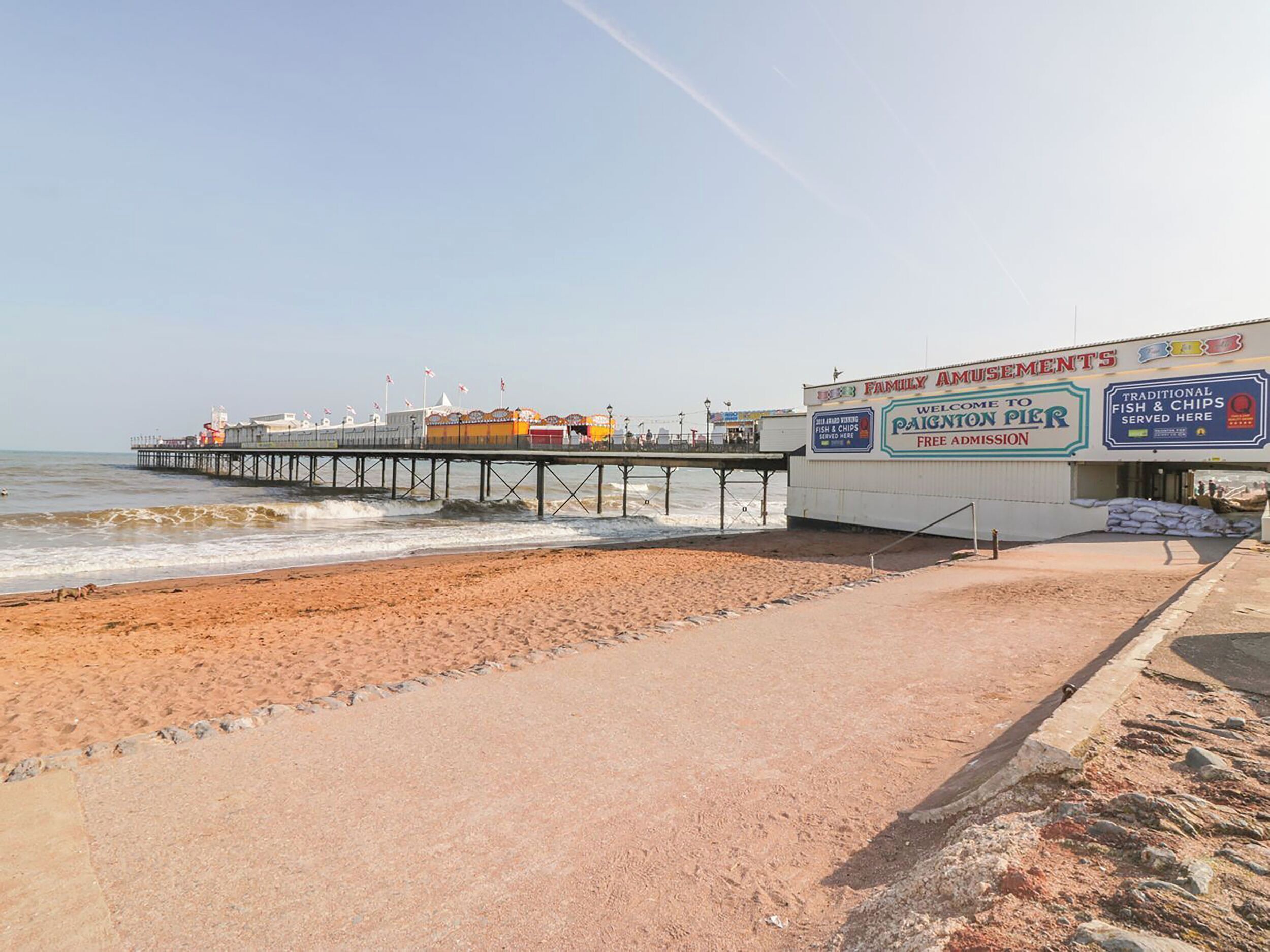A beach with a pier extending into the water, a building with a sign for 'Family Amusements' and 'Welcome to Paginton Pier', and a sandy beach area.