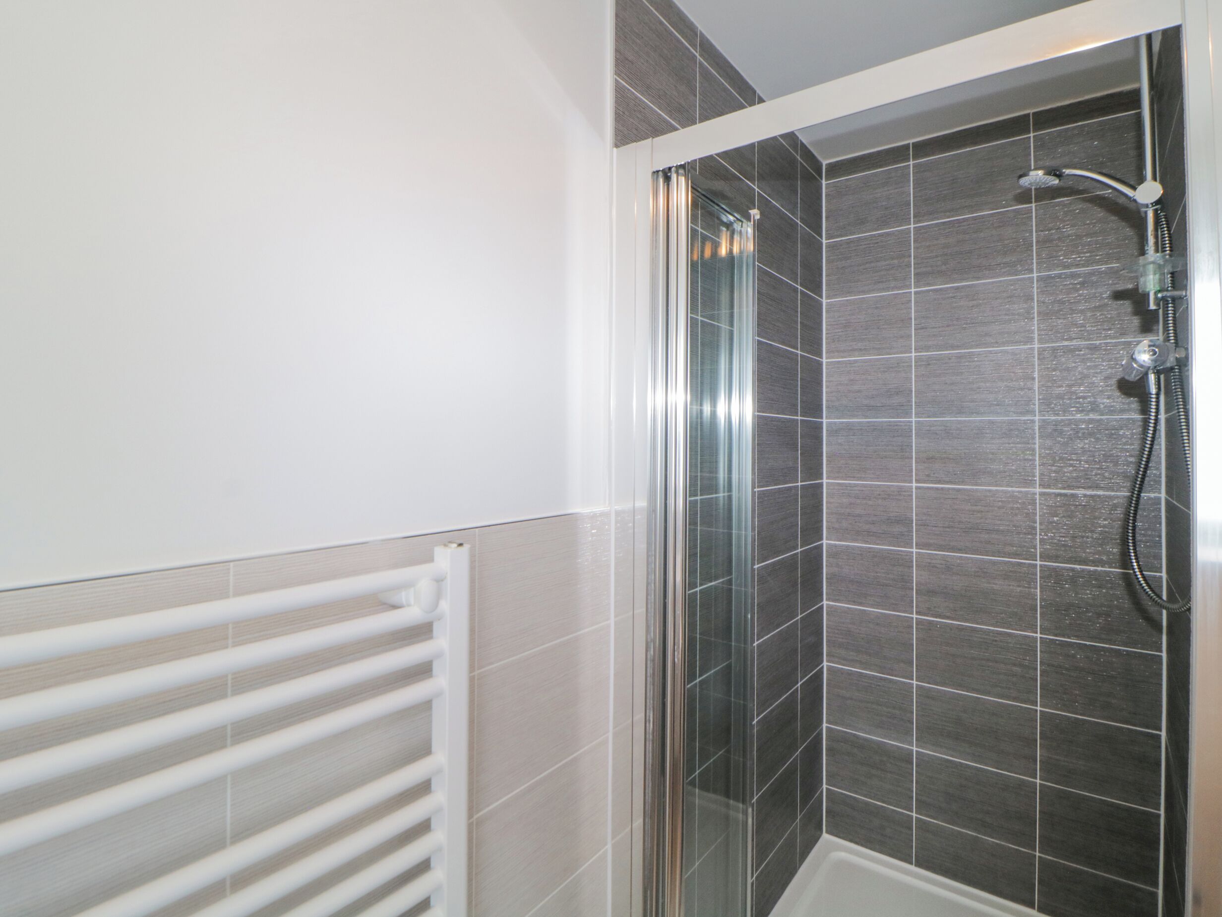 A shower with a glass door, tiled walls, and a white radiator.