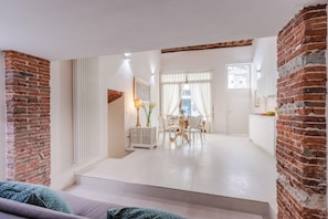 A modern living space with exposed brick walls, a dining area with white furniture, and a kitchen area with white cabinets.