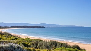 A coastal landscape with a sandy beach, clear blue sea, and distant mountains.