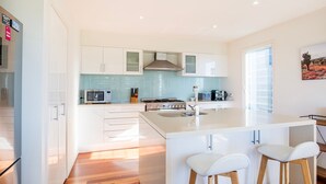 A modern kitchen with white cabinetry, a central island with stools, a microwave, a stove, and a coffee maker.