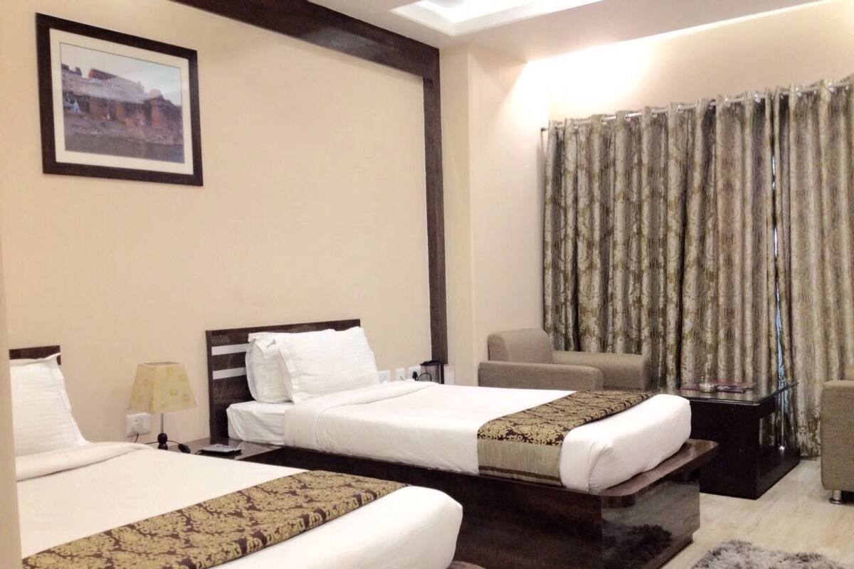 Habitación de hotel con dos camas, un escritorio, una silla y un ventanal grande con cortinas.