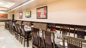A dining area with long wooden tables and chairs, framed artwork on the walls, and a modern ceiling design. - Hotel Madhuvan Palace (Varanasi)