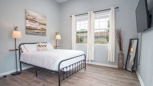 A bedroom with a bed, two bedside lamps, a window with curtains, a painting on the wall, and a television mounted on the wall. - Charming 3br/2ba Gem Close to Downtown/ Riverwalk (San Antonio)