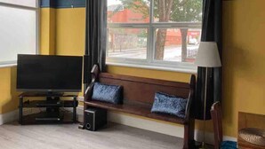 A room with a large window, a television, a bench with cushions, and a lamp. - Sleeps 14 Cardiff City Centre (Cardiff)