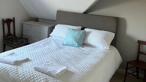 A bedroom with a sloped ceiling, a bed with white bedding, a nightstand, a dresser, and two chairs. - Sleeps 14 Cardiff City Centre (Cardiff)