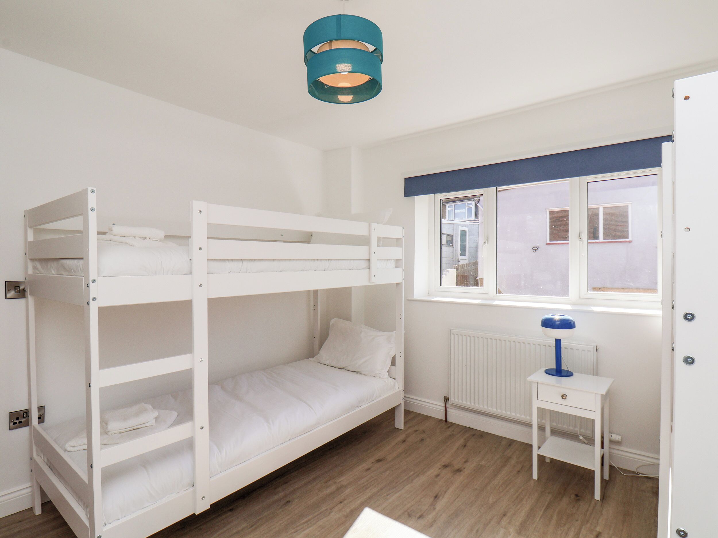 A bunk bed room with a window, a radiator, and a small table with a lamp.