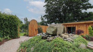Een rustiek houten gebouw met een grote boog en een tuin met rotsen en begroeiing.