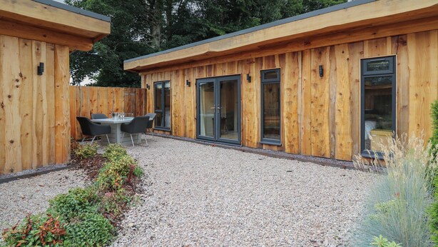 Een houten chalet met een grindpad, een eettafel met stoelen en een kleine tuin.