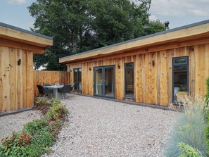 A wooden cabin with a gravel patio, a dining table with chairs, and a small garden area. - Rhosyn (Welshpool)