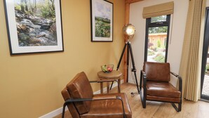 Een kamer met twee leren fauteuils, een bijzettafeltje met een schaal fruit, en ingelijste foto's aan de muur.