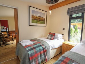 A bedroom with a bed, a bedside table, a window with a view of greenery, a framed picture on the wall, and a door leading to another room. - Pansi (Welshpool)