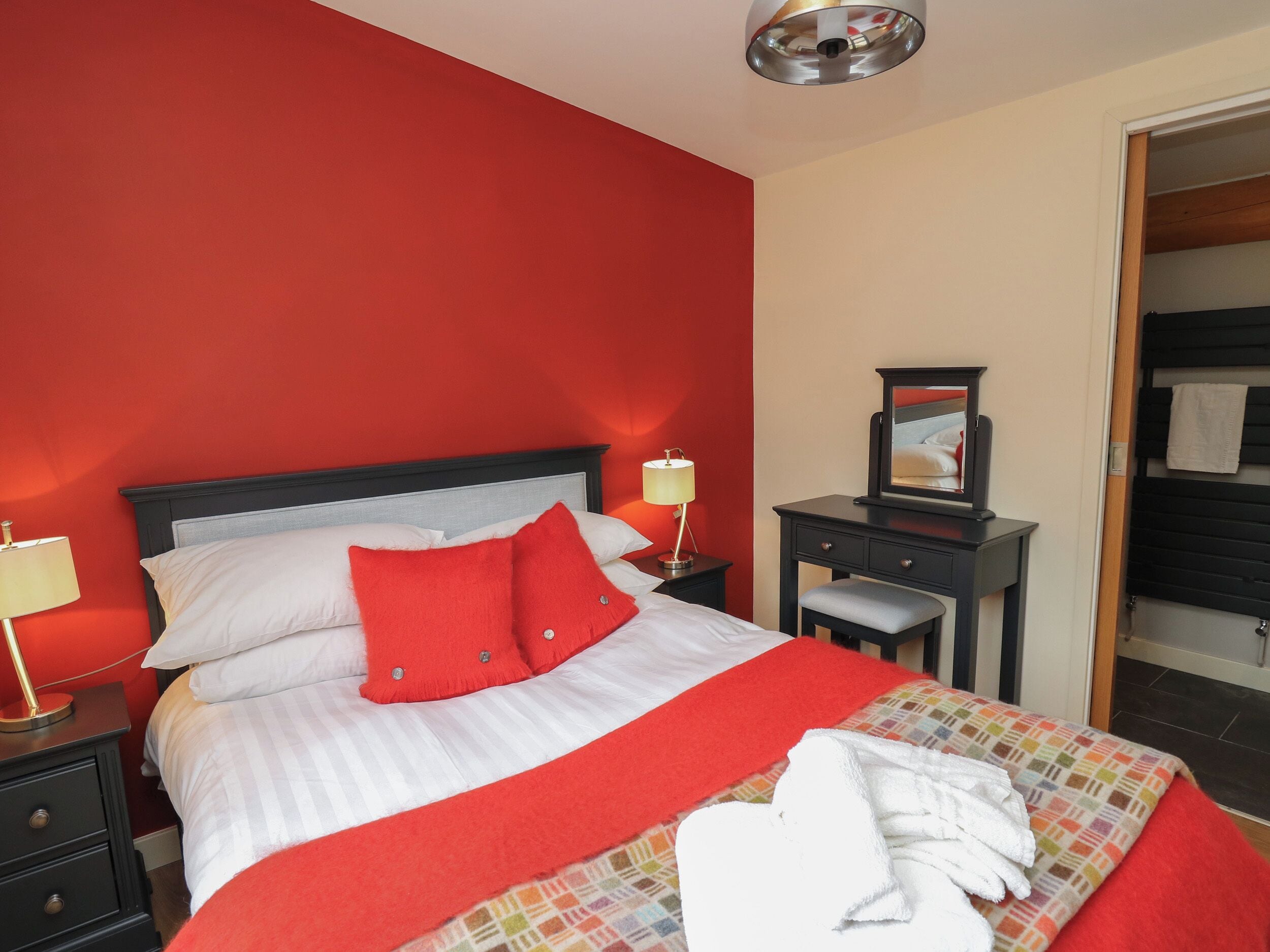 Una habitación de hotel con cama, mesita de noche con lámpara, cómoda y espejo.