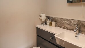 A bathroom with a white sink, a mirror, and toiletries on the countertop. - Fioled (Welshpool)