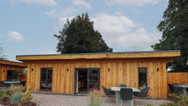 A wooden cabin with a dining area and a kitchen visible through the open door. - Fioled (Welshpool)