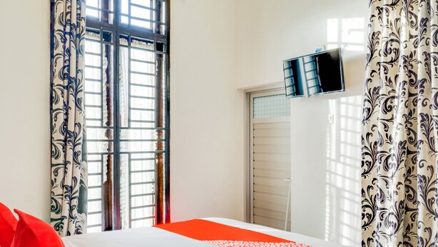 A hotel room with a bed, curtains, a TV mounted on the wall, and a window with a view. - OYO 3015 Galliano Homestay Syariah (Bukittinggi)