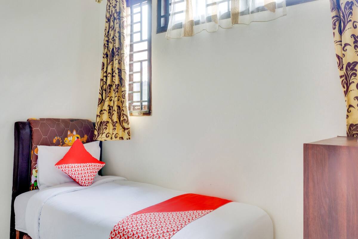 A neatly made bed with patterned bedding, a headboard with a decorative panel, and a window with patterned curtains.