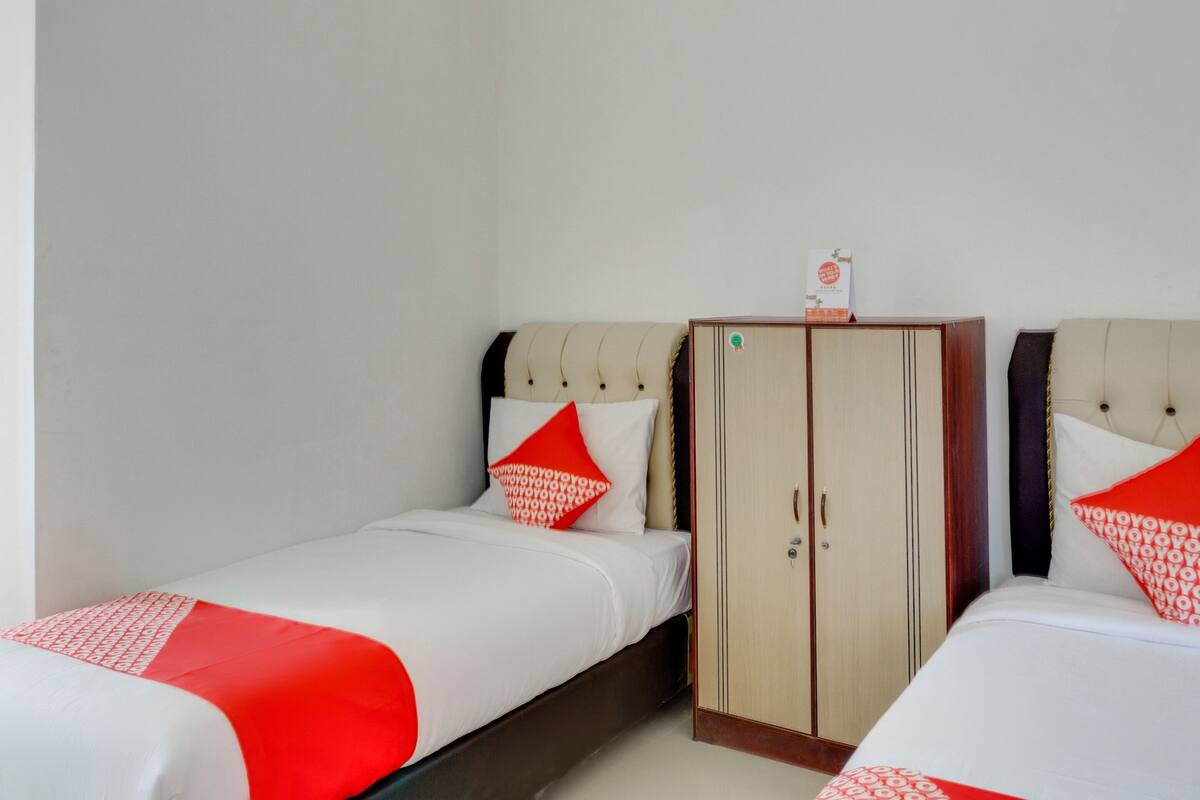 A hotel room with two single beds, each with a red and white bedspread, and a wooden wardrobe with a mirror.
