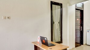 A clean, modern hotel room with a wooden desk, a laptop, and a door leading to a kitchen area. - OYO 3015 Galliano Homestay Syariah (Bukittinggi)